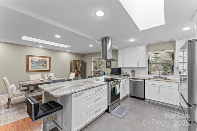 kitchen featuring a sink, a skylight, stainless steel appliances, a peninsula, and range hood