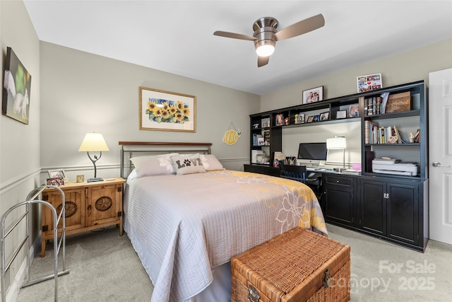 bedroom with ceiling fan, a wainscoted wall, and light carpet