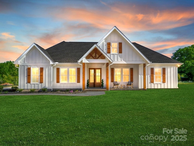 back of property at dusk with board and batten siding, a lawn, and roof with shingles