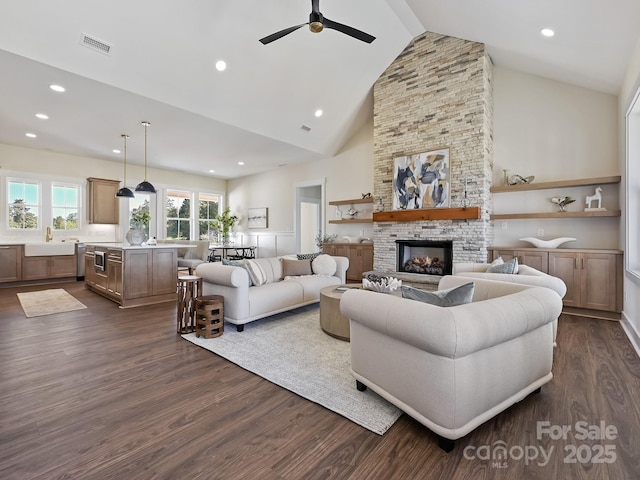 living area with dark wood-style flooring, visible vents, a ceiling fan, a fireplace, and high vaulted ceiling