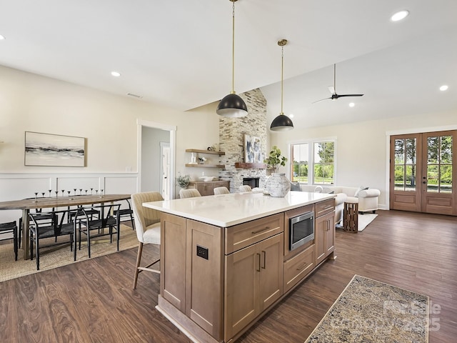 kitchen featuring a stone fireplace, a ceiling fan, stainless steel microwave, open floor plan, and dark wood-style flooring