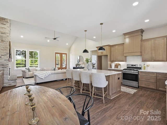 kitchen with stainless steel range with gas cooktop, light countertops, a kitchen bar, dark wood finished floors, and lofted ceiling