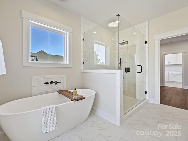 bathroom with marble finish floor, baseboards, a freestanding bath, and a stall shower