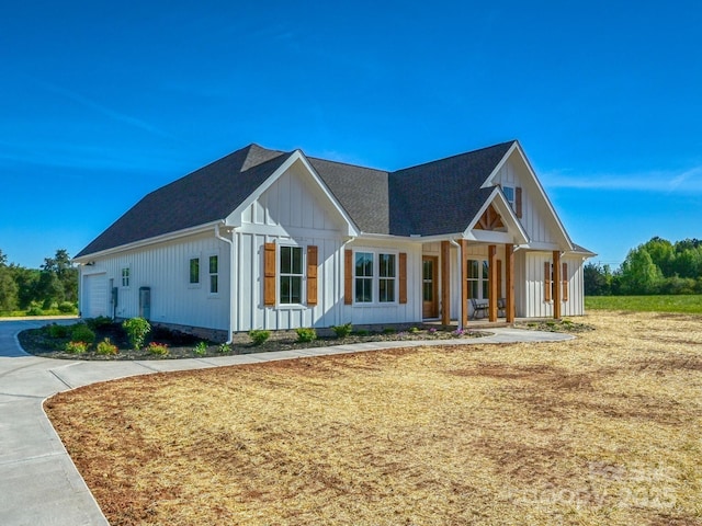modern inspired farmhouse featuring board and batten siding, an attached garage, driveway, a porch, and roof with shingles