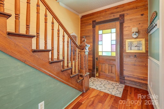 foyer featuring stairs, wood finished floors, wooden walls, and crown molding