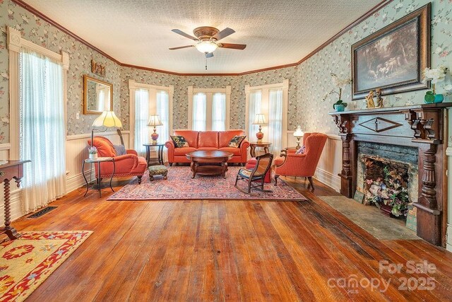 living area featuring hardwood / wood-style flooring, visible vents, ceiling fan, wallpapered walls, and ornamental molding