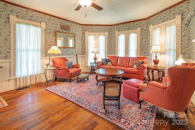 living area with a wainscoted wall, ceiling fan, hardwood / wood-style flooring, and ornamental molding