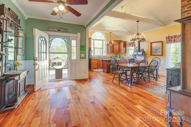 foyer entrance featuring light wood-style floors, lofted ceiling with beams, crown molding, wainscoting, and ceiling fan with notable chandelier