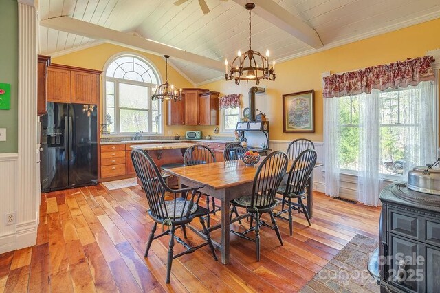 dining area with lofted ceiling with beams, a chandelier, light wood-type flooring, and wainscoting