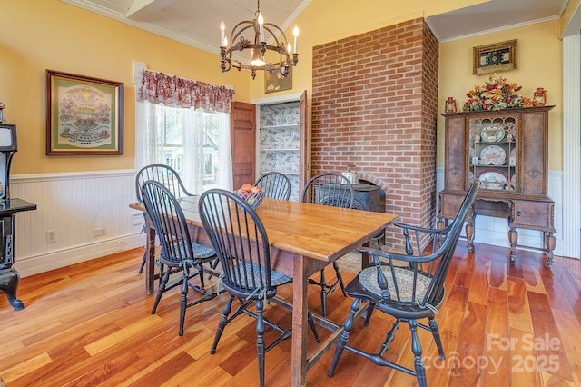 dining area with crown molding, a notable chandelier, wainscoting, and wood finished floors