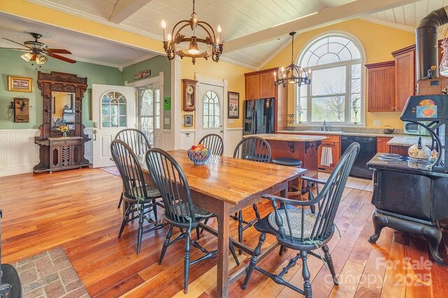 dining area with crown molding, lofted ceiling with beams, a wainscoted wall, light wood finished floors, and ceiling fan with notable chandelier