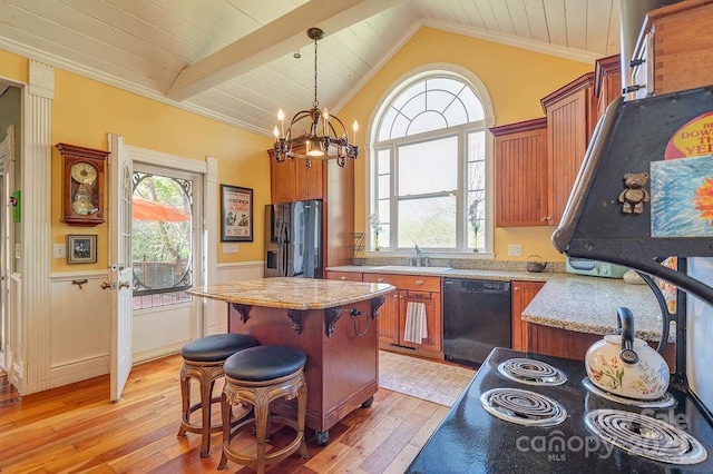 kitchen with a sink, light wood-style floors, black appliances, a wainscoted wall, and a kitchen island