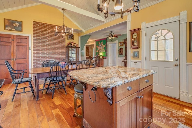 kitchen featuring pendant lighting, light wood-style flooring, lofted ceiling with beams, a kitchen bar, and ceiling fan with notable chandelier