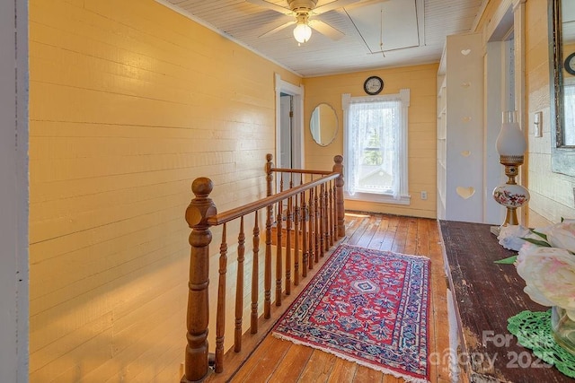 corridor featuring an upstairs landing, attic access, wooden walls, and hardwood / wood-style flooring