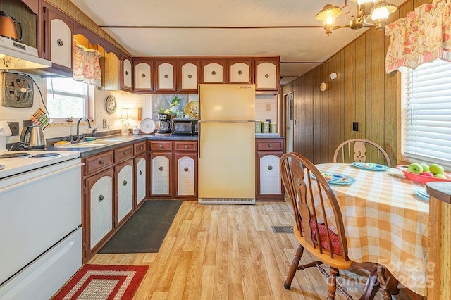 kitchen featuring white appliances, light wood-style flooring, decorative backsplash, wood walls, and a sink
