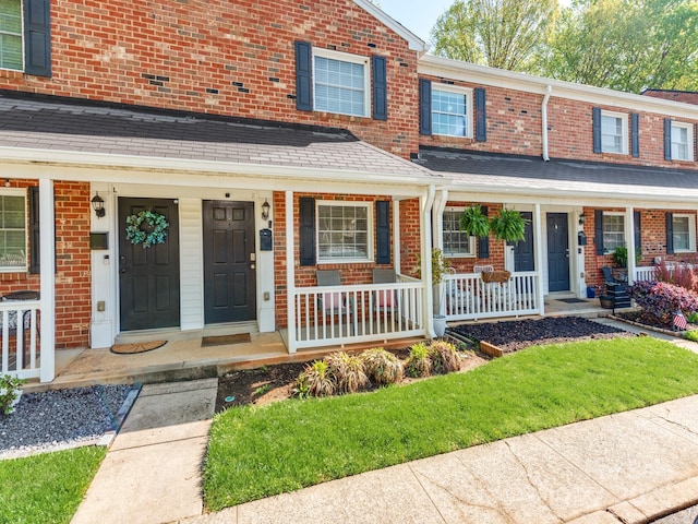 view of property featuring brick siding, a porch, and roof with shingles