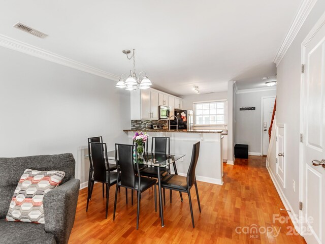 dining room featuring an inviting chandelier, light wood finished floors, ornamental molding, and visible vents