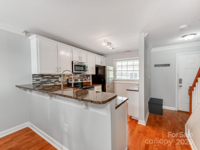 kitchen with a peninsula, white cabinetry, dark stone countertops, appliances with stainless steel finishes, and backsplash