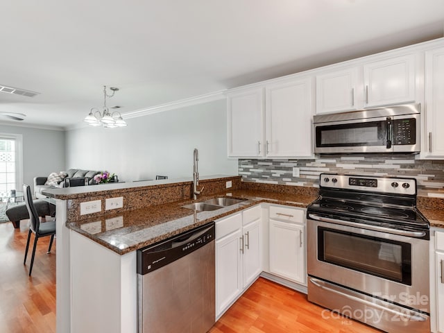 kitchen featuring ornamental molding, a peninsula, visible vents, stainless steel appliances, and a sink