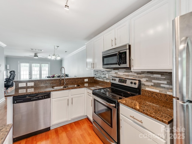 kitchen with a peninsula, white cabinetry, crown molding, appliances with stainless steel finishes, and a sink