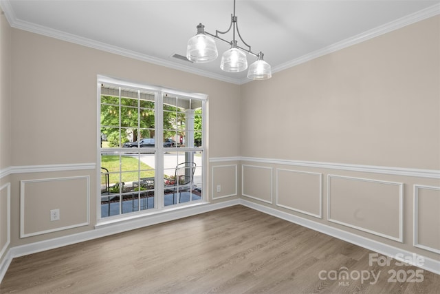 empty room featuring wainscoting, a decorative wall, wood finished floors, visible vents, and ornamental molding