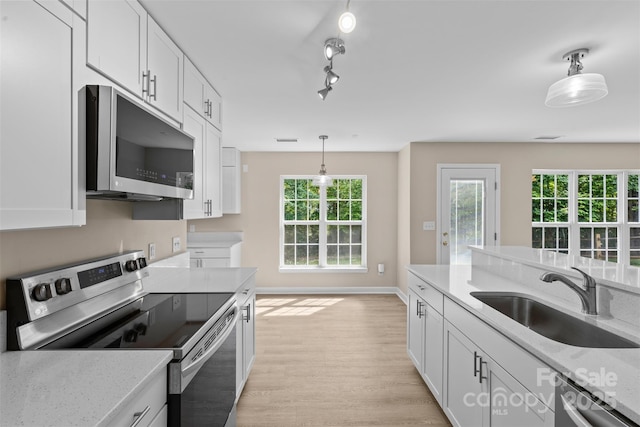 kitchen featuring pendant lighting, light wood-style floors, white cabinetry, a sink, and stainless steel appliances