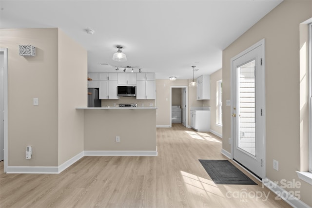 kitchen with washer / clothes dryer, white cabinets, a peninsula, stainless steel appliances, and light wood-style flooring