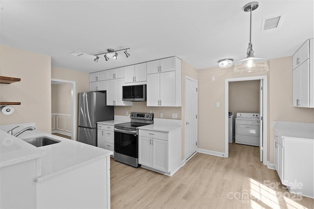 kitchen featuring washing machine and dryer, white cabinetry, a sink, light wood finished floors, and appliances with stainless steel finishes