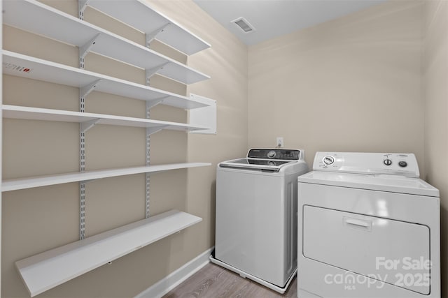 laundry area featuring laundry area, visible vents, washing machine and clothes dryer, wood finished floors, and baseboards