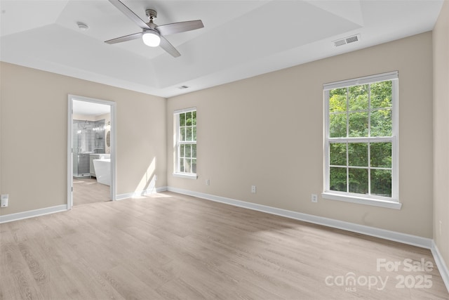 spare room featuring visible vents, baseboards, ceiling fan, a tray ceiling, and light wood-style flooring