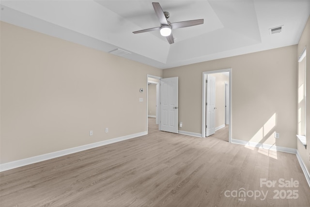 unfurnished bedroom featuring baseboards, a tray ceiling, light wood-style flooring, and visible vents