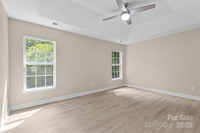 empty room with visible vents, light wood-style floors, baseboards, ceiling fan, and a raised ceiling