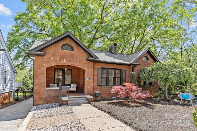 view of front facade with covered porch, roof with shingles, fence, brick siding, and a chimney