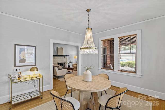 dining area featuring a notable chandelier, baseboards, ornamental molding, a brick fireplace, and wood finished floors