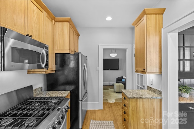 kitchen featuring light wood-style flooring, light brown cabinetry, light stone counters, stainless steel appliances, and baseboards