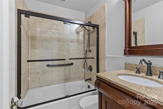 full bathroom with combined bath / shower with glass door, vanity, wainscoting, and toilet