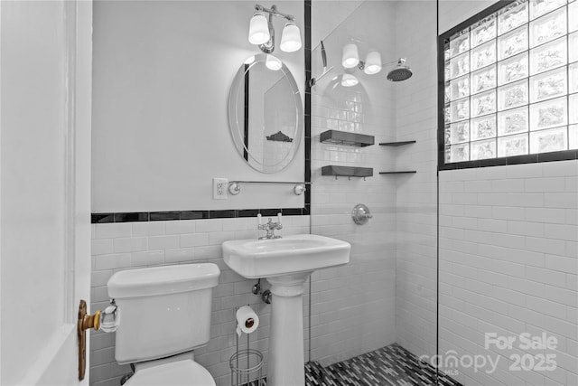 bathroom featuring wainscoting, tile walls, a tile shower, and toilet