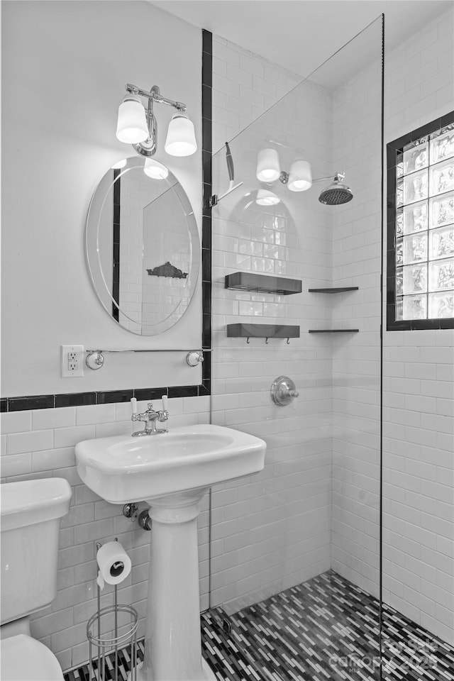 full bath featuring tile walls, toilet, a stall shower, and wainscoting