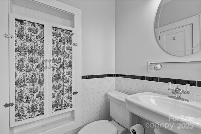 bathroom with toilet, a sink, wainscoting, and tile walls