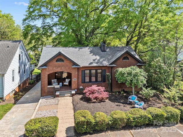 view of front facade with brick siding, a chimney, and a shingled roof