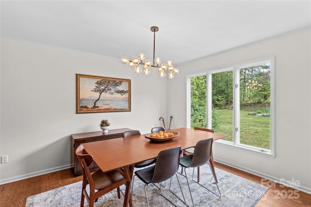 dining room featuring baseboards, ornamental molding, an inviting chandelier, and light wood-style floors