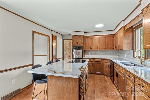 kitchen with crown molding, a sink, visible vents, light wood-style floors, and black appliances