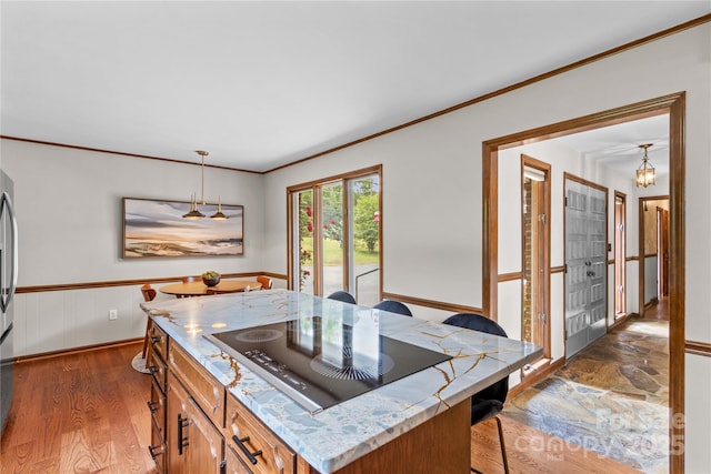 kitchen featuring wood finished floors, black electric stovetop, wainscoting, brown cabinets, and crown molding