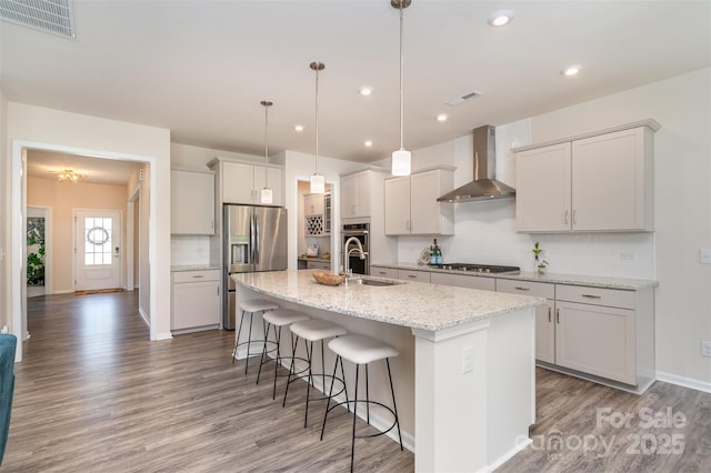 kitchen with visible vents, a sink, wall chimney range hood, a kitchen breakfast bar, and stainless steel appliances