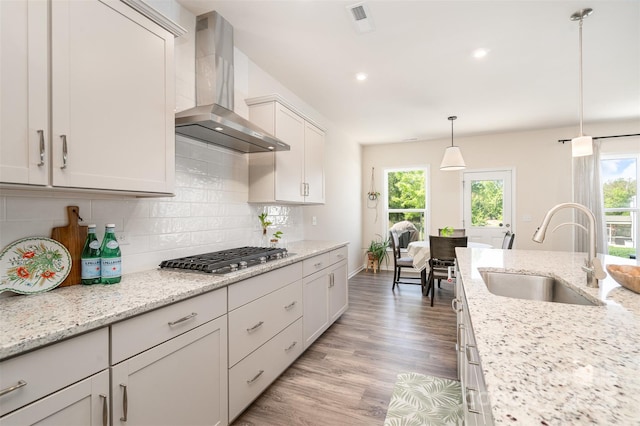 kitchen featuring plenty of natural light, backsplash, stainless steel gas cooktop, wall chimney exhaust hood, and a sink