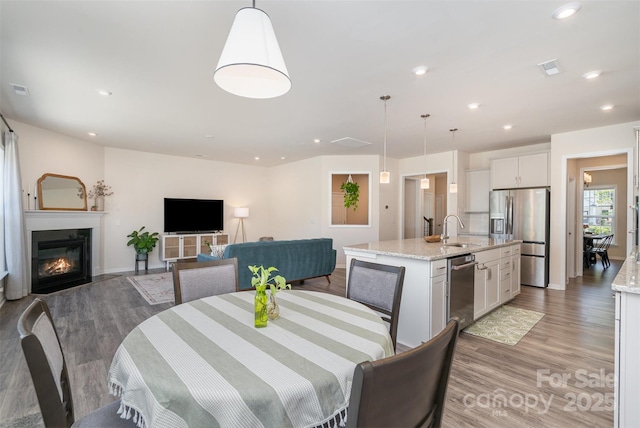 dining area with visible vents, light wood-type flooring, a glass covered fireplace, and recessed lighting