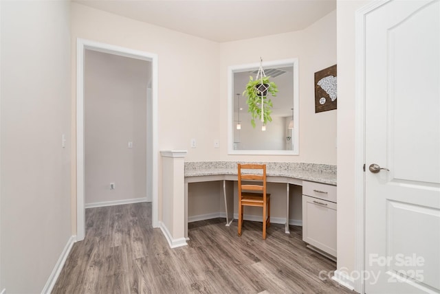 unfurnished office featuring baseboards, light wood finished floors, and built in study area