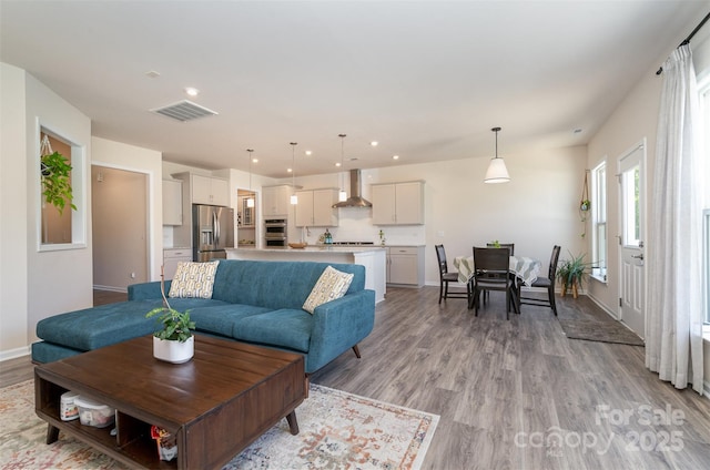 living area featuring visible vents, light wood-style flooring, recessed lighting, and baseboards