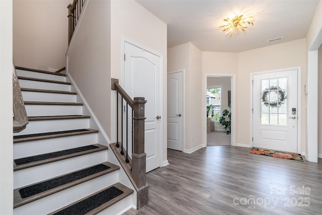 foyer entrance with wood finished floors, baseboards, visible vents, and stairs