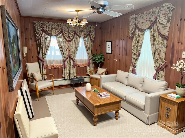 living room with a baseboard heating unit, wood walls, crown molding, and ceiling fan with notable chandelier